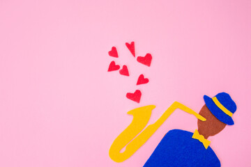 Silhouette of a musician with a saxophone on a pink background, cutted out of felt. International Jazz Day. Copy space. Flat lay