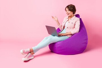 Full size photo of young happy smiling girl sit armchair having video conference in laptop isolated on pink color background