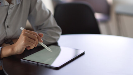 Businessperson hand with stylus pen touching on mock-up tablet screen on round table