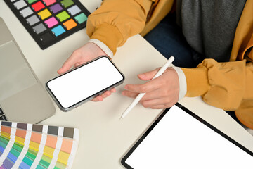 Female designer hands working with smartphone on office desk with tablet and designer supplies