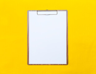 Wooden clipboard with blank paper white paper on yellow fabric background, blank paper sheet, office tool
