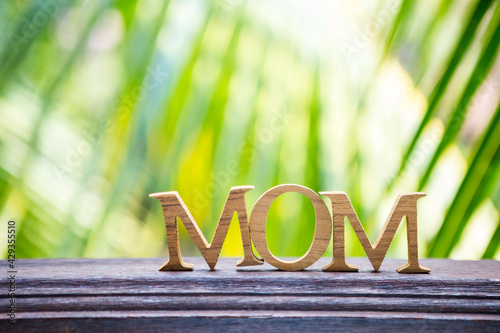 Happy Mother's day card background idea, mom wooden font over blurred natural green background, outdoor day light