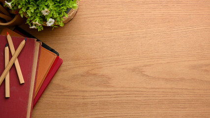 Wooden study table with books, coloured pencils, plant pot and copy space