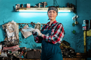Portrait of a young smiling female mechanic in uniform, wearing gloves. Working room in the background. The concept of gender equality