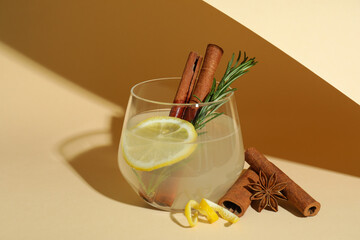 Glass of lemonade with cinnamon and rosemary on beige background