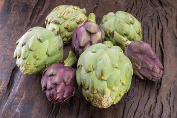 Obraz premium Green and purple artichoke flower edible buds on wooden background.