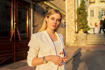 Portrait of young beautiful woman in white jacket looking at camera in sunset