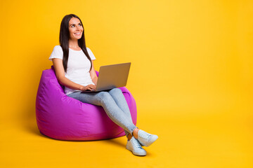 Photo of shiny young lady wear white t-shirt sitting beanbag typing modern gadget looking empty space isolated yellow color background