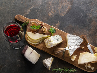 Cheese platter with organic cheeses, fruits, nuts and wine on stone background. Top view. Tasty cheese starter.