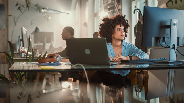 Creative Office: Young Black Woman Sitting at Her Desk Working on Computer. Charmingly Authentic Software Developer, Social Media Marketing Specialist Creating Content, Using Devices. Wide Shot