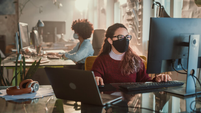 Creative Office: Hispanic Woman Wearing Face Mask Sitting at Her Desk Working on Computer. Charmingly Authentic Professional Wearing Stylish Glasses Creates Social Media Business Marketing Campaign
