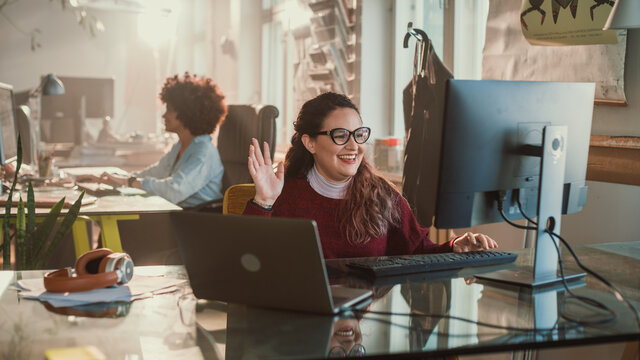 Creative Office: Hispanic Woman Making Video Call on Computer, Greeting Colleagues. Charming Professional Wearing Stylish Glasses Creates Social Media Business Marketing Campaign
