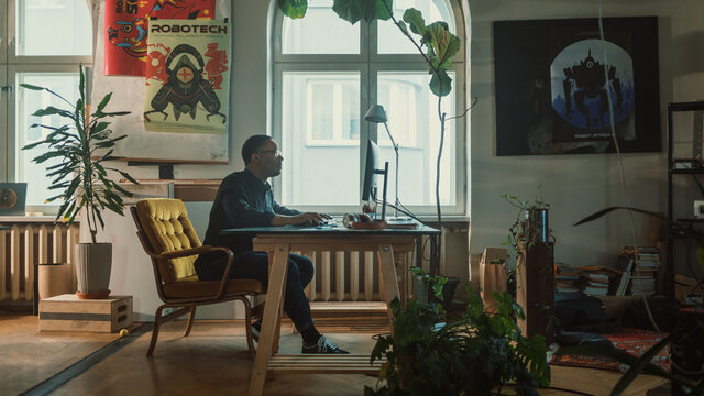 Handsome Black Male Specialist Sitting at His Desk Works on Computer in Creative Office. Professional works on Mobile Software Development, App Design, Social Media Project. Side Medium Portrait
