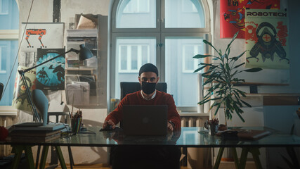 Young Specialist Wearing Face Mask Sitting at His Desk Works on Computer in Creative Office. Professional works on Software Development Project, Game App Design, Social Media Marketing. Medium Shot
