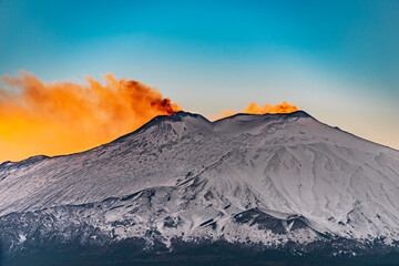 Red glow on the top of Mt Etna during sunset. Orange smoke and blue sky 
