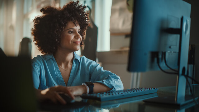 Creative Office: Young Black Woman Sitting at Her Desk Working on Computer, Greeting Colleague with Smiles. Authentic Software Developer, Social Media Marketing Specialist Creating Content. Wide Shot