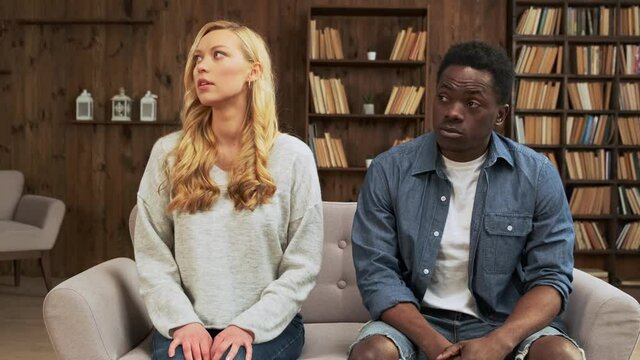 Upset mixed race ethnicity young couple sit separate turn back on sofa avoid talk after fight conflict, interracial upset husband and wife think of divorce