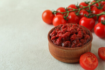 Wooden bowl with tomato paste and tomatoes on white textured table