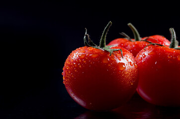 Fresh red tomatoes with drops of water on black background.