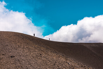 People on the edge of a volcanic crater, blue sky in the background 