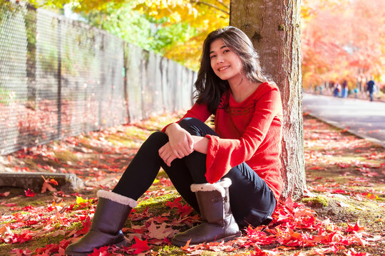 Teen girl in red shirt sitting under colorful maple tree