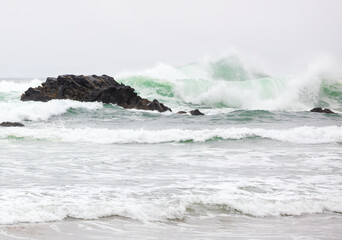 Beautiful emerald green waves of Pacific Ocean hitting rocky shore
