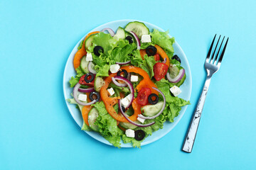 Plate of greek salad and fork on blue background
