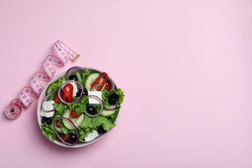Bowl of greek salad and measuring tape on pink background
