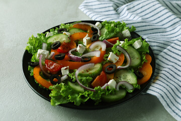 Plate of greek salad and kitchen towel on white textured background