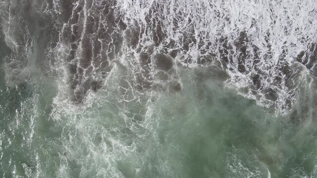 Aerial view to waves in beach splashing with dark sand. Blue turquoise  clean wavy sea water.
