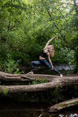 Blonde woman in sportswear practicing breathing yoga on a log over the forest river. Fitness girl doing a stretching exercise outdoor in harmony with nature.