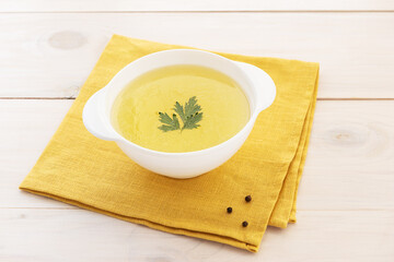 Bone broth with parsley in a bowl on a yellow napkin.