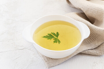 Homemade chicken bone broth with parsley in a white bowl with a towel.