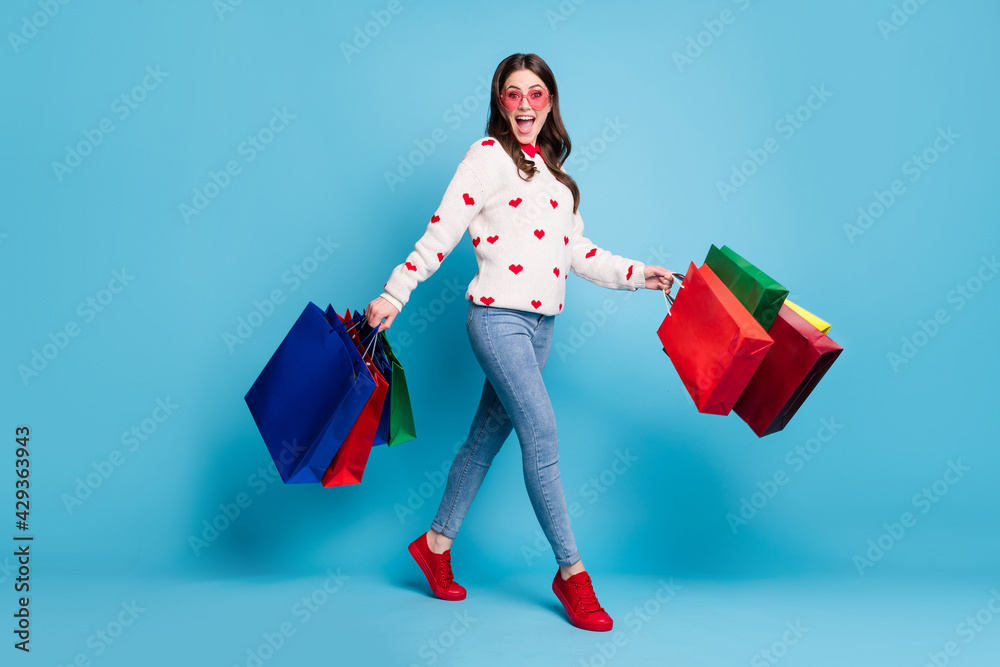 Wall mural Full length photo of impressed young lady wear hearts print sweater glasses walking arms bargains isolated blue color background