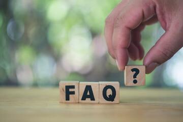 Man hand puts wooden cubes with question marks near the word FAQ.