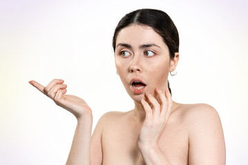 Portrait of a surprised Caucasian woman pointing her finger to the side. Light background. Banner. The concept of skin care and cosmetic procedures