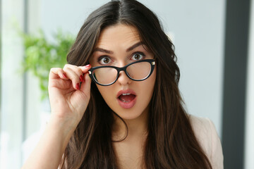 Young surprised woman adjusting glasses for vision