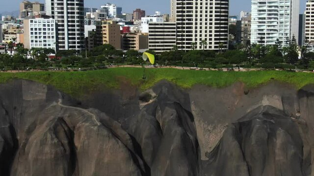 4k daytime aerial video of a paraglider flying very close to the coastline of Lima, Peru, in the Miraflores area. Truck left to right, 30 fps. Recreational paragliding