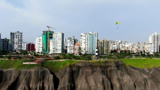4k aerial daytime video of 2 people paragliding over the coast of Miraflores, Lima, right near Antonio Raimondi Park and Navy Lighthouse (Faro de la Marina) in Peru. Pan left to right, 30fps