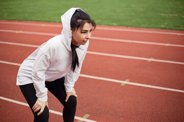 Obraz premium Running track treadmill, on the start. Sporty weary woman preparing for marathon triathlone. Female tired exhausted prostration runner training on the stadium. Image copy space 
