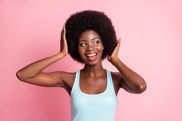 Portrait of optimistic brunette curly lady hand hair look empty space wear blue top isolated on pink color background