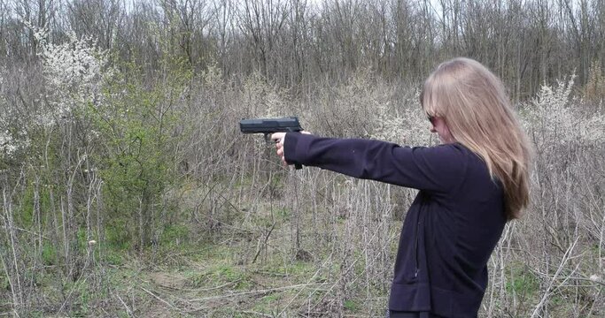 Young blond woman practicing target shooting with a gun rear side view unrecognizable