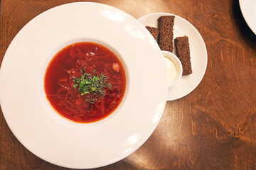 A traditional dish of Russian and Ukrainian cuisine. Borscht with herbs, sour cream and garlic croutons. On a wooden table with copy space