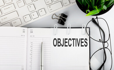 Text OBJECTIVES on white stickers on the notebook with keyboard and glasses.