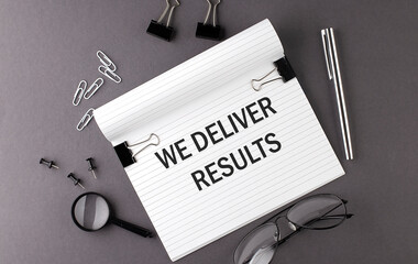 Text WE DELIVER RESULTS on Notebook and office tools on gray desktop