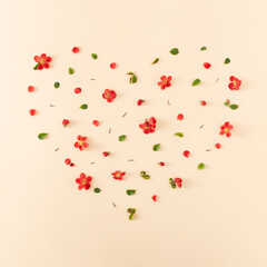 Heart shaped floral pattern made with red flowers, petals, green leaves and thorns on bright beige background. Creative spring nature arrangement. Flat lay.