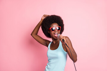Photo of funky charming dark skin young lady hold mic singer wear sunglass karaoke isolated on pink...