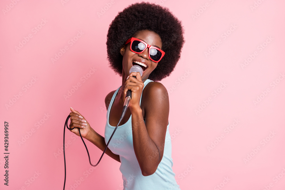 Wall mural Photo of happy funky dark skin young woman hold sing mic music lover isolated on pink color background