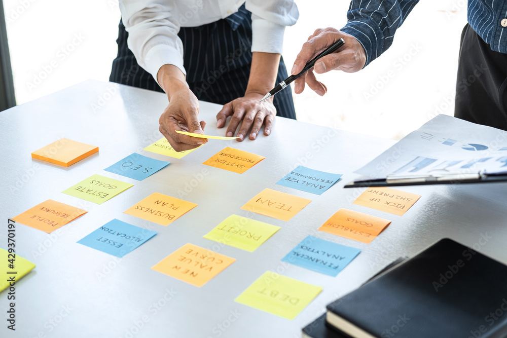 Fototapete Two creative business people meeting and planning use note on desk to share idea, Analysis data chart and graph with teamwork strategy brainstorming in office