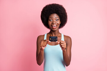 Photo of amazed afro american woman wear blue tank-top hold credit card isolated on pink color background